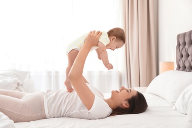 Young mother playing with her cute baby on bed indoors