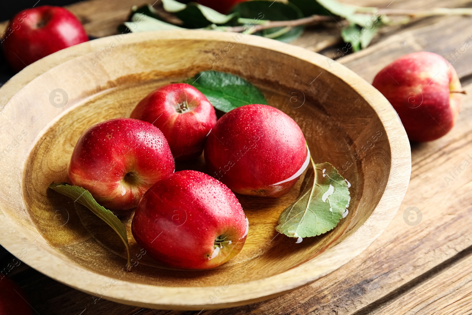 Photo of Ripe red apples in bowl of water on wooden table, closeup