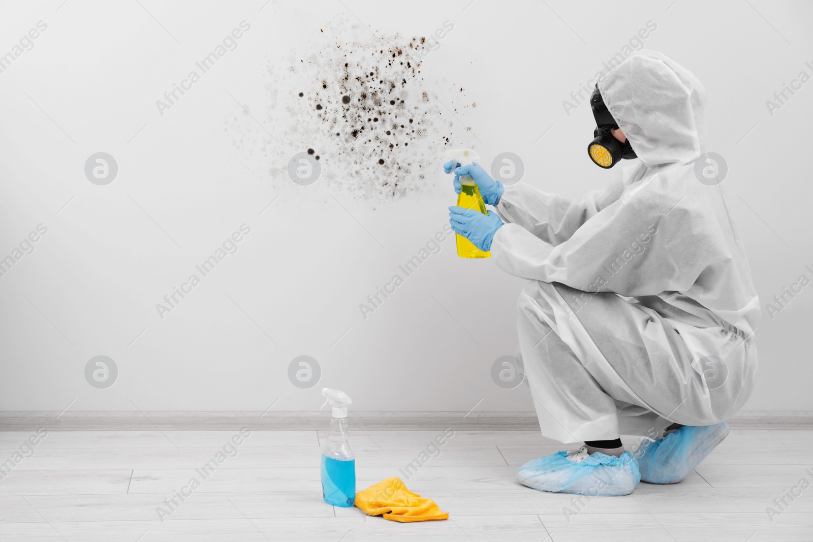 Image of Woman in protective suit and rubber gloves using mold remover on wall