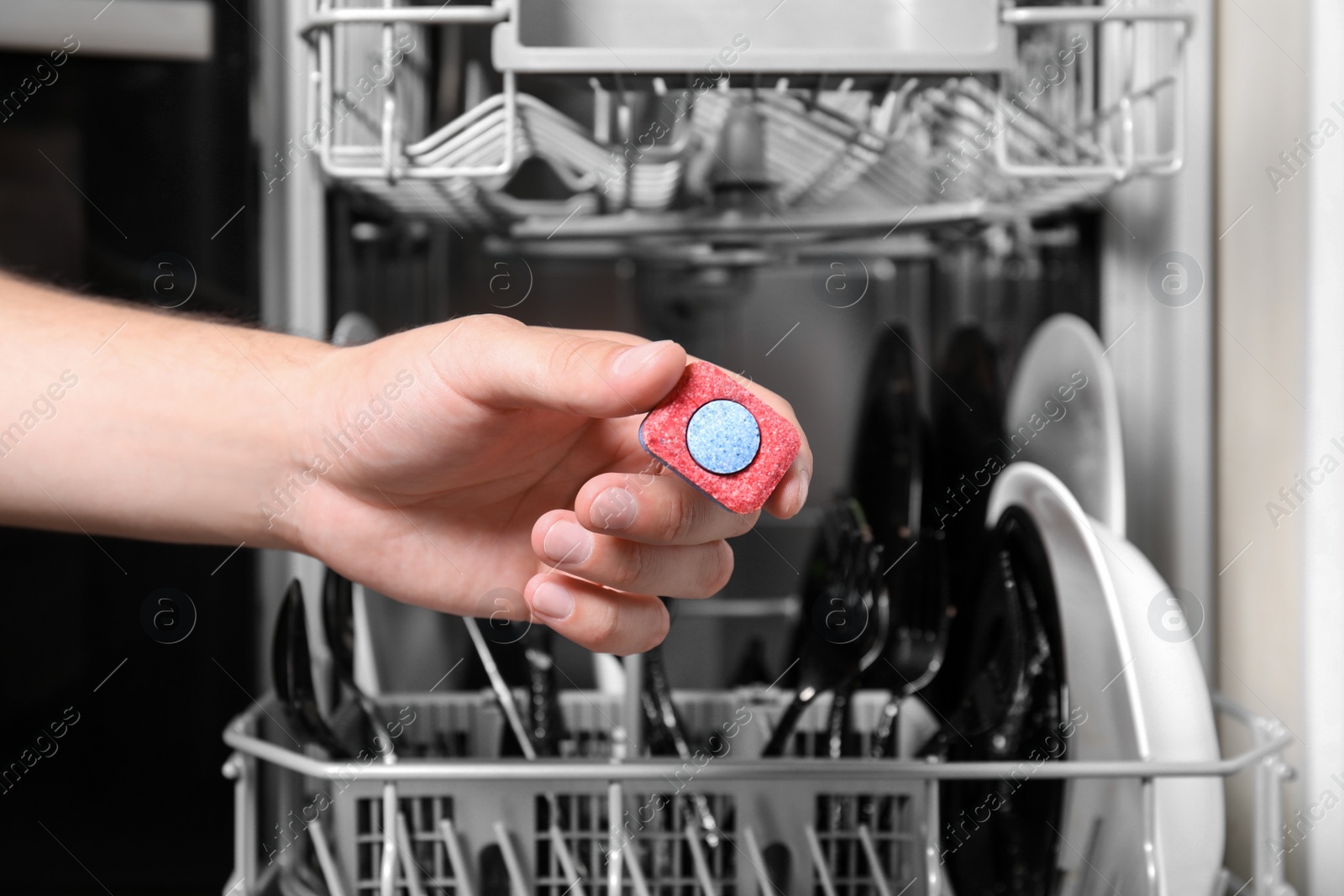 Photo of Woman putting detergent tablet into open dishwasher in kitchen, closeup