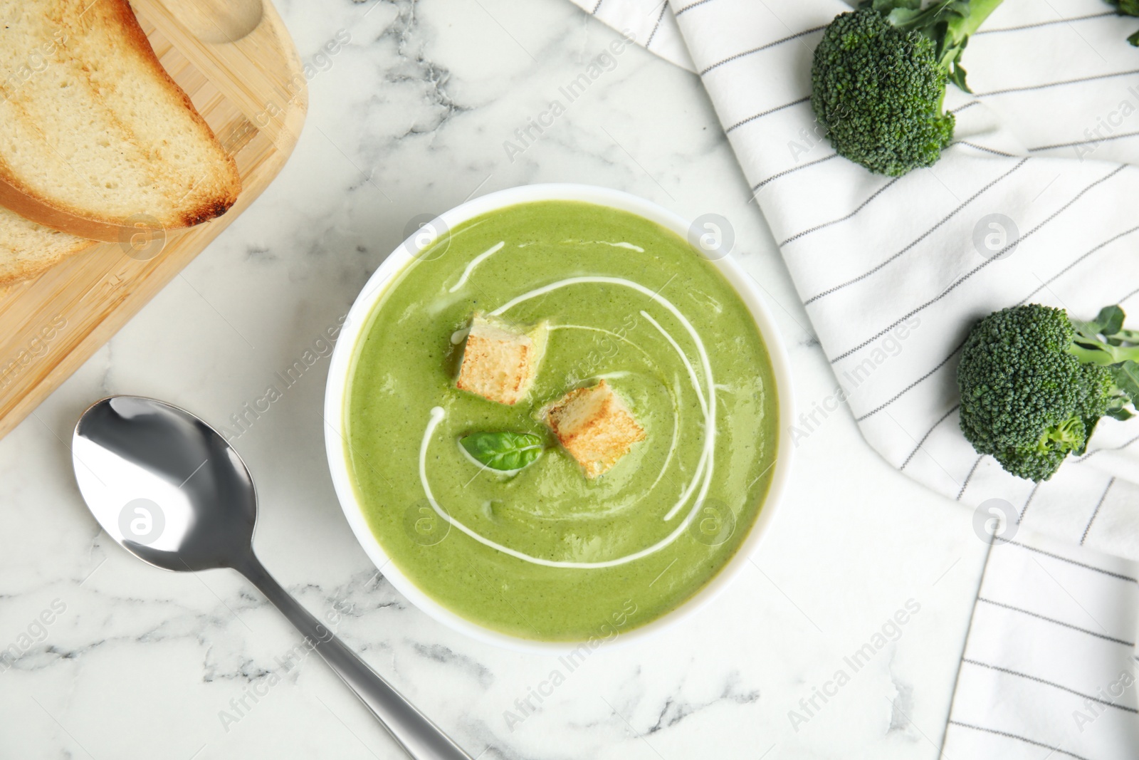 Photo of Delicious broccoli cream soup with croutons served on white marble table, flat lay