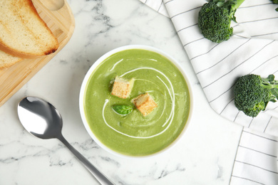 Delicious broccoli cream soup with croutons served on white marble table, flat lay