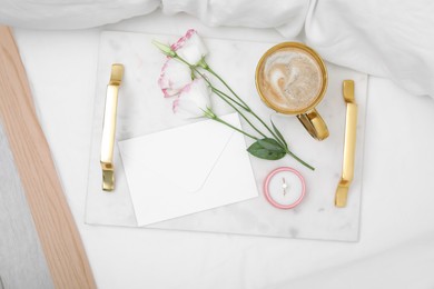 Photo of Tray with cup of coffee, flowers and beautiful engagement ring in box on white bed, top view