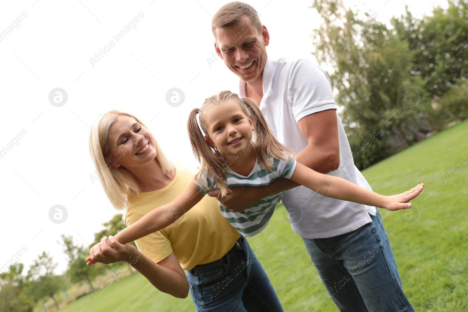 Photo of Cute little girl having fun with her parents in park on summer day