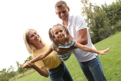 Cute little girl having fun with her parents in park on summer day