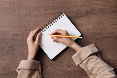 Woman writing in notebook at wooden table, top view