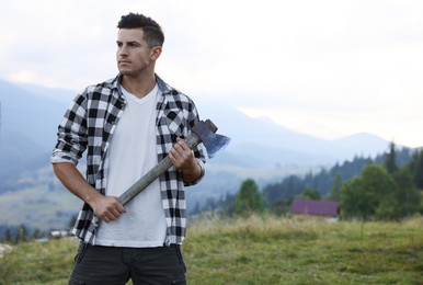 Handsome man with axe in mountains, space for text