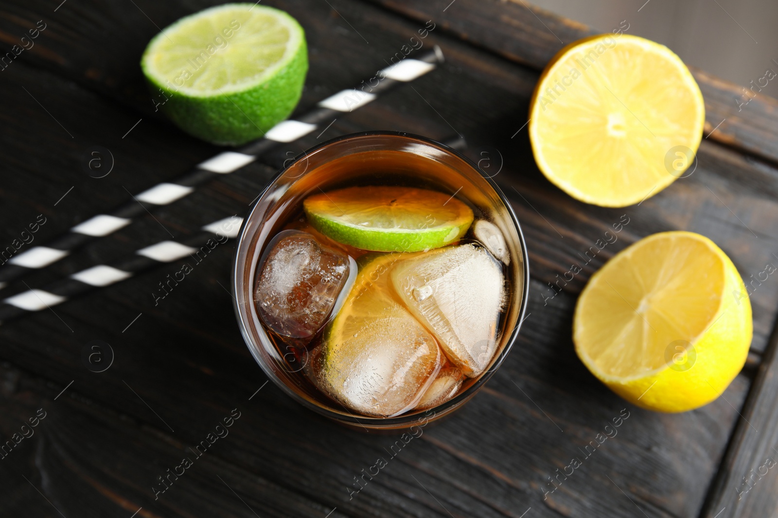 Photo of Glass of cocktail with cola, ice and cut lime on wooden table, flat lay