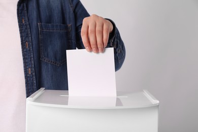 Woman putting her vote into ballot box on light grey background, closeup