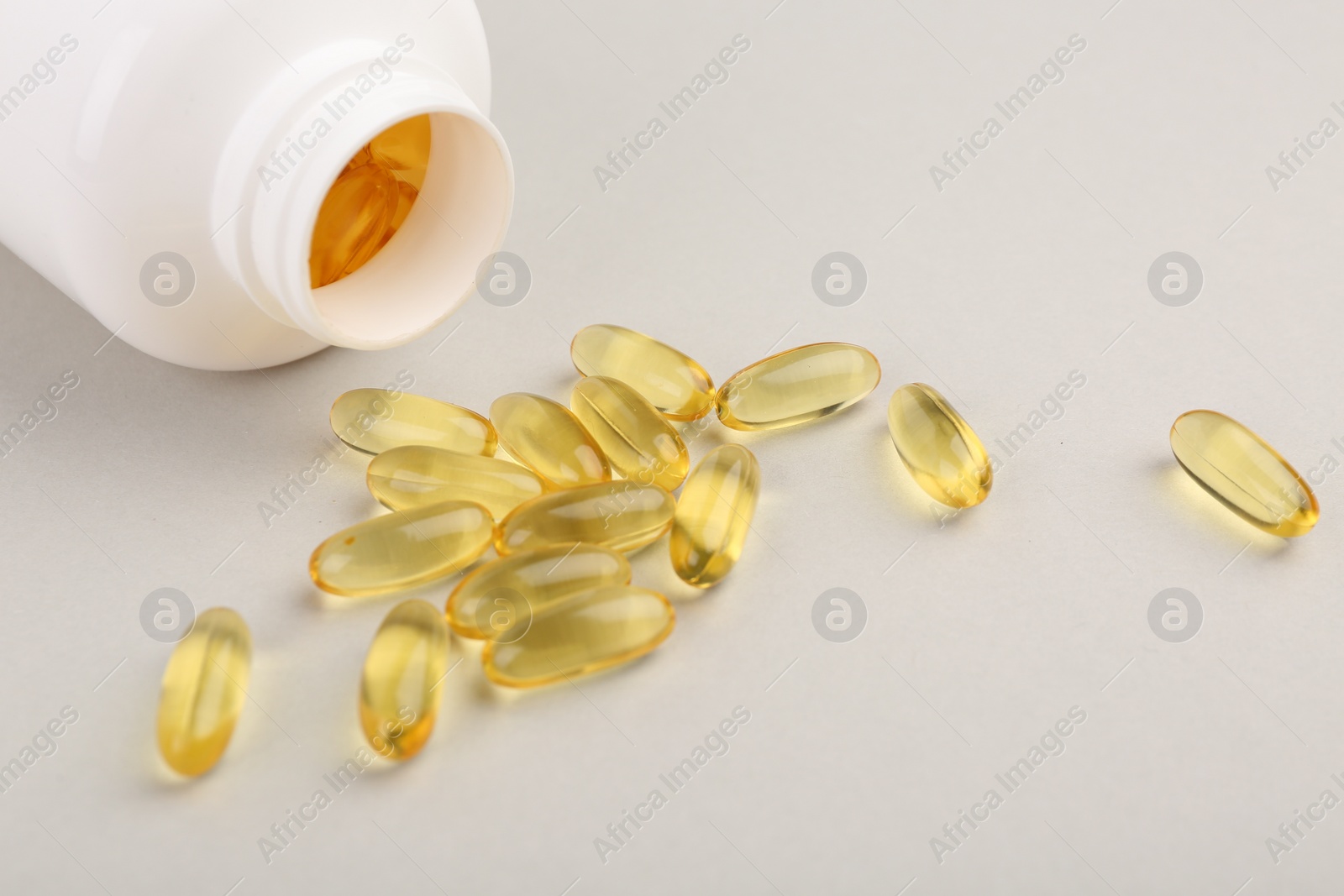 Photo of Vitamin capsules and bottle on light grey background, closeup