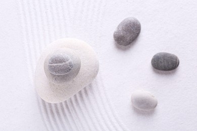 Photo of Zen garden stones on white sand with pattern, flat lay