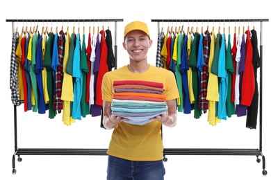 Image of Dry-cleaning delivery. Happy courier holding folded clothes near wardrobe racks on white background
