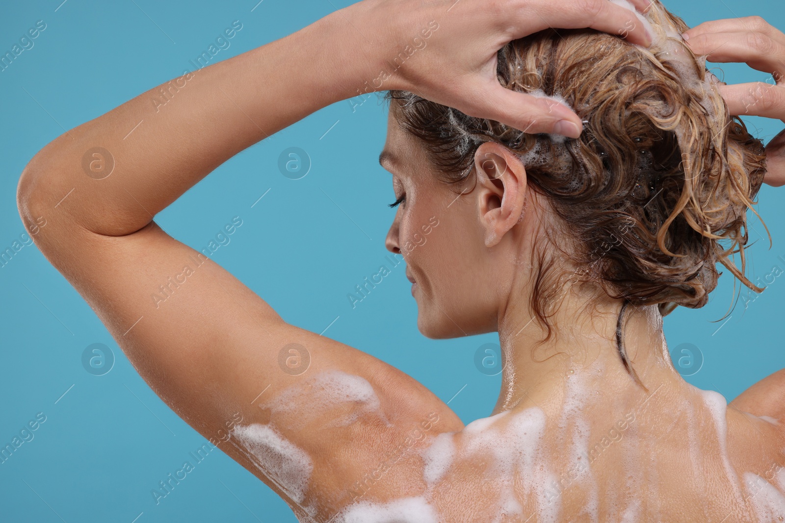 Photo of Woman washing hair on light blue background, back view