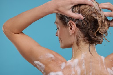 Woman washing hair on light blue background, back view