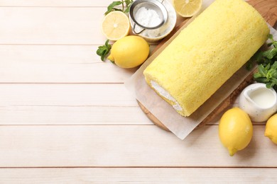 Photo of Delicious cake roll, lemons, mint and powdered sugar on light wooden table, flat lay. Space for text