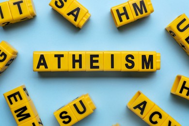 Word Atheism made of yellow cubes with letters on light blue background, flat lay