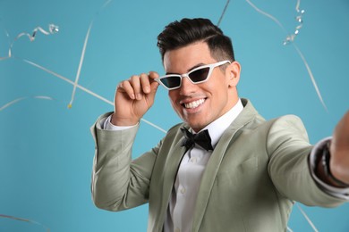 Photo of Happy man taking selfie and falling down serpentines on light blue background