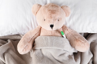Photo of Toy bear with thermometer lying in bed, top view. Children's hospital