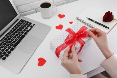 Photo of Woman with gift box at white table, closeup. Valentine's day celebration