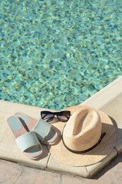 Stylish sunglasses, slippers and straw hat at poolside on sunny day, space for text. Beach accessories
