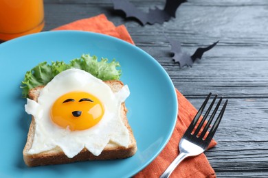 Photo of Halloween themed breakfast served on black wooden table, closeup. Tasty toast with fried egg in shape of ghost
