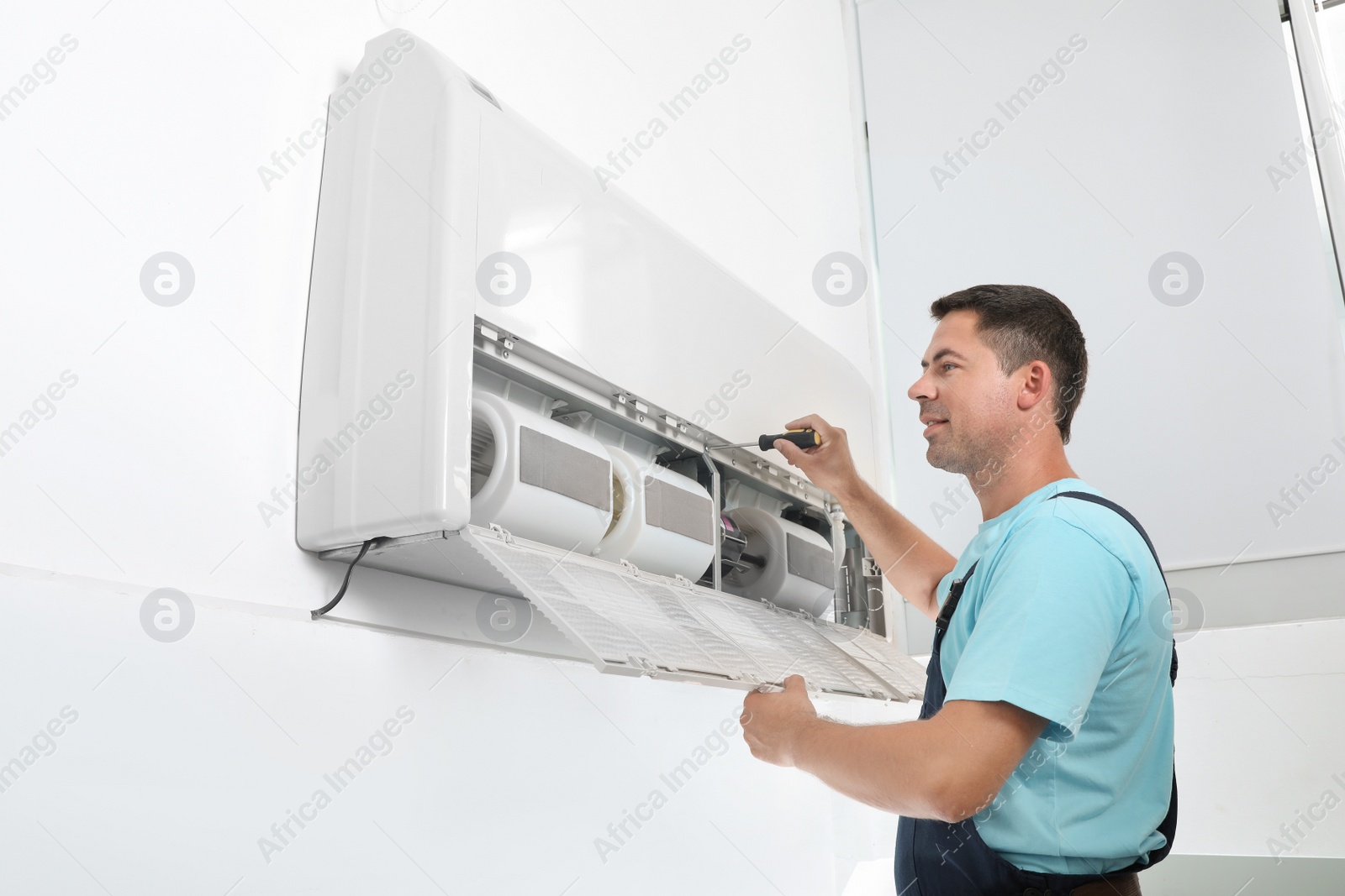 Photo of Male technician fixing modern air conditioner indoors