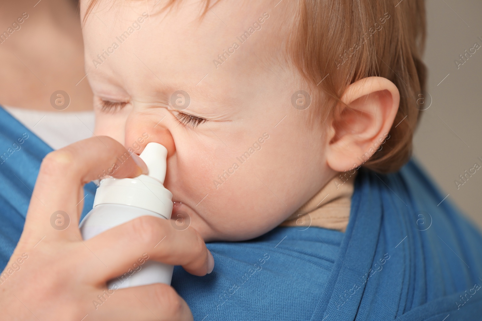 Photo of Mother helping her baby to use nasal spray, closeup
