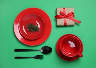 Beautiful Christmas table setting with gift on green background, flat lay