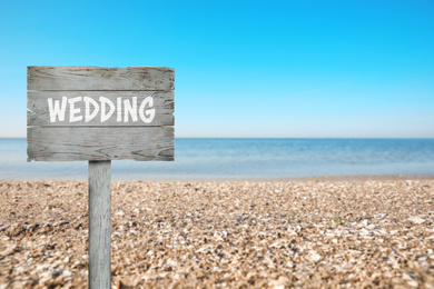 Wooden plaque with inscription Wedding on sandy beach, space for text 