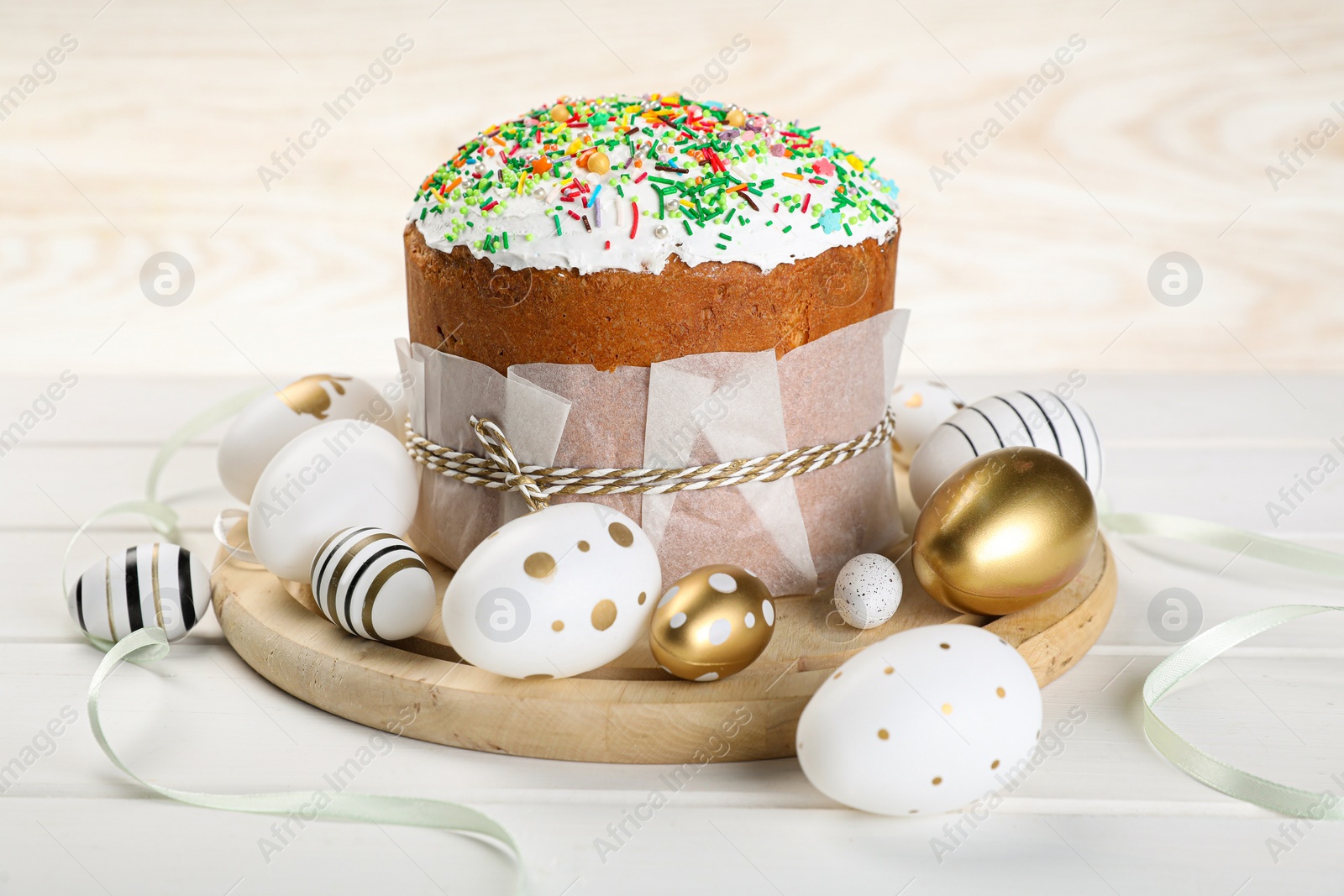 Photo of Traditional Easter cake with sprinkles and painted eggs on white wooden table