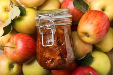 Photo of Delicious apple jam in jar on fresh fruits, top view