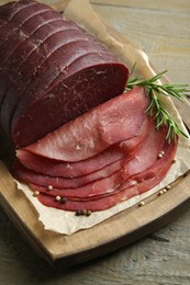 Photo of Tasty bresaola, peppercorns and rosemary on wooden table, closeup