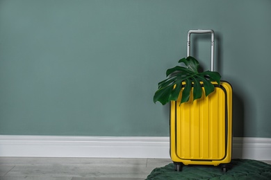 Photo of Bright yellow suitcase with tropical leaf near color wall indoors