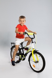 Cute little boy riding bicycle on grey background