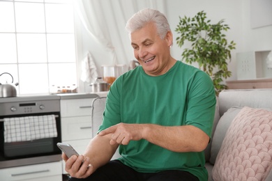 Mature man laughing while using smartphone at home