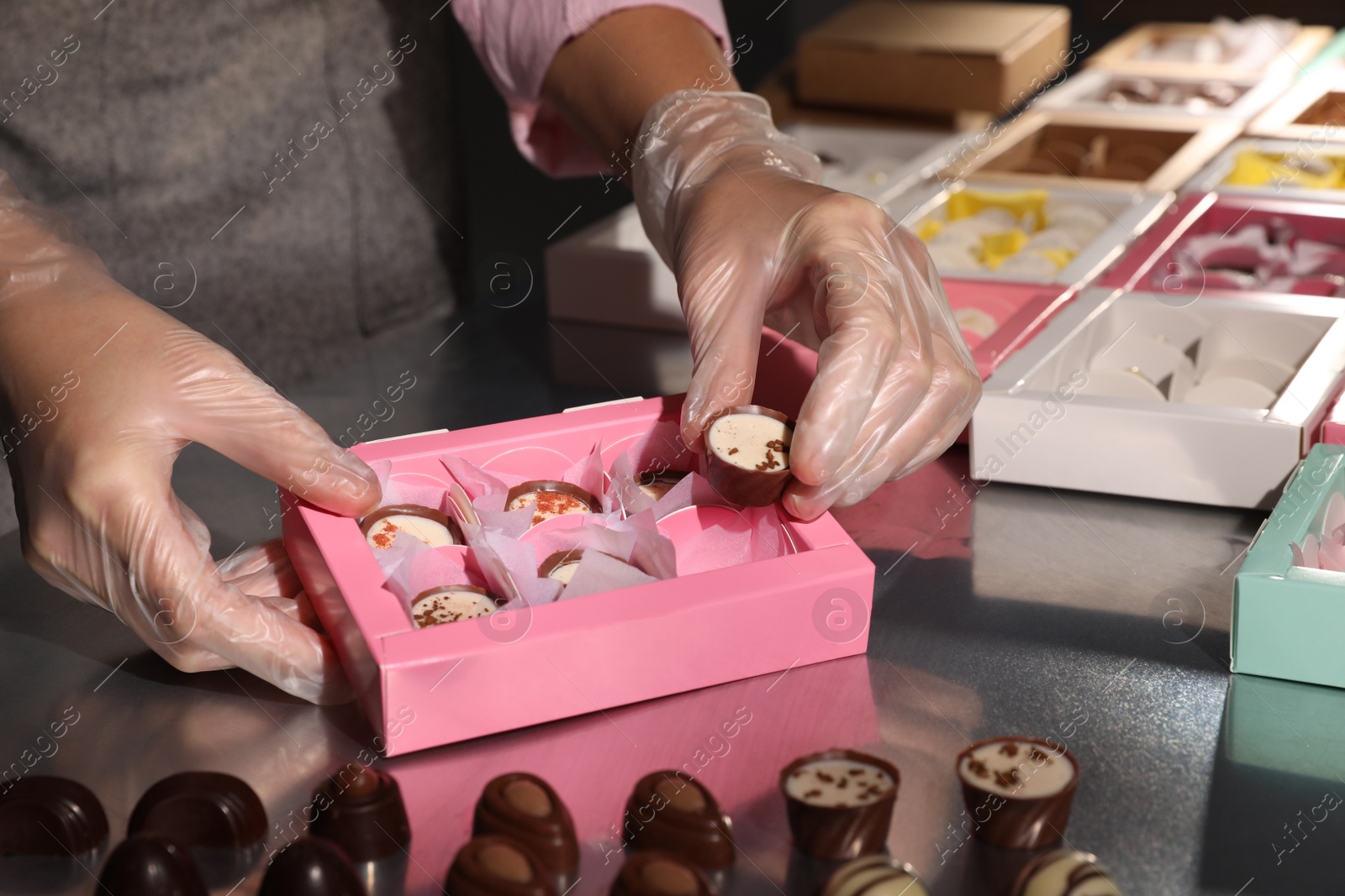 Photo of Woman packing delicious candies into pink box at production line, closeup