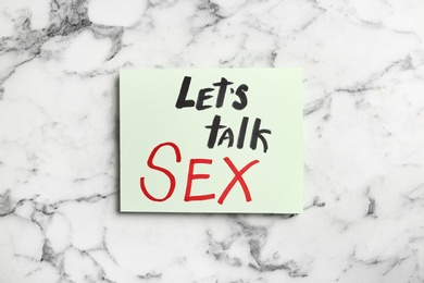 Photo of Note with phrase "LET'S TALK SEX" on marble background, top view
