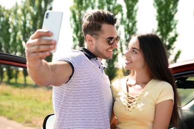 Happy young couple taking selfie near car on road