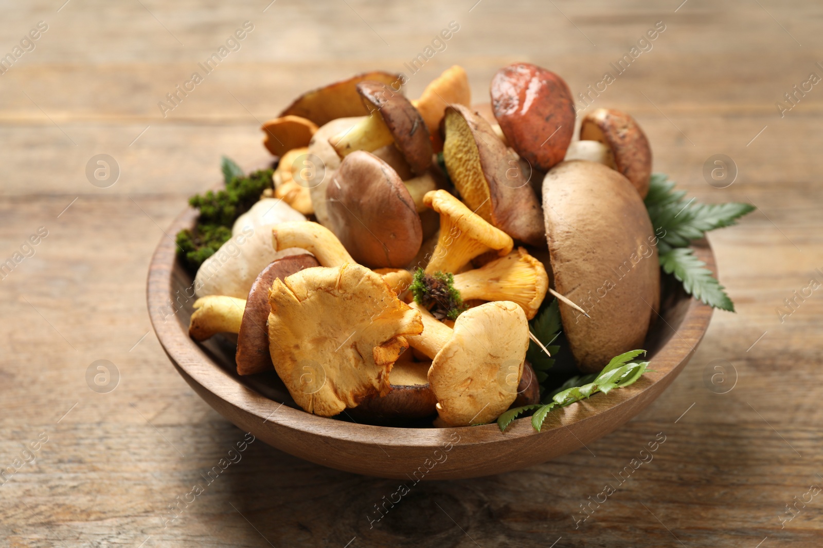 Photo of Bowl with different mushrooms on wooden table