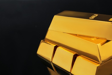 Photo of Stack of shiny gold bars on black background, closeup. Space for text