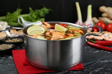 Photo of Saucepan with delicious Tom Yum soup and ingredients on black marble table