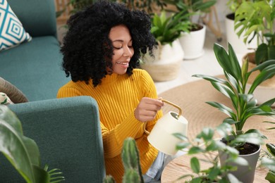 Photo of Happy woman watering beautiful potted houseplants at home