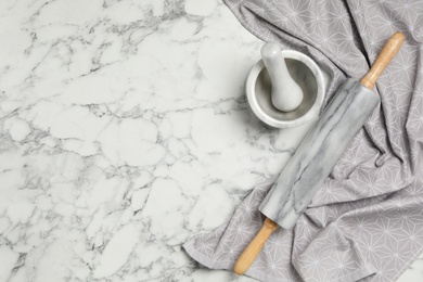 Rolling pin, mortar and pestle on white marble table, flat lay with space for text. Cooking utensils