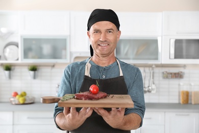 Photo of Professional male chef holding board with meat in kitchen