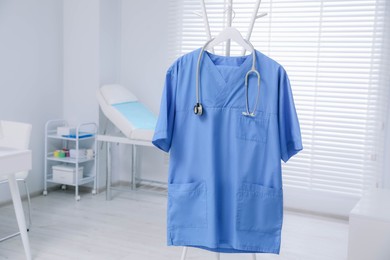 Photo of Blue medical uniform and stethoscope hanging on rack in clinic