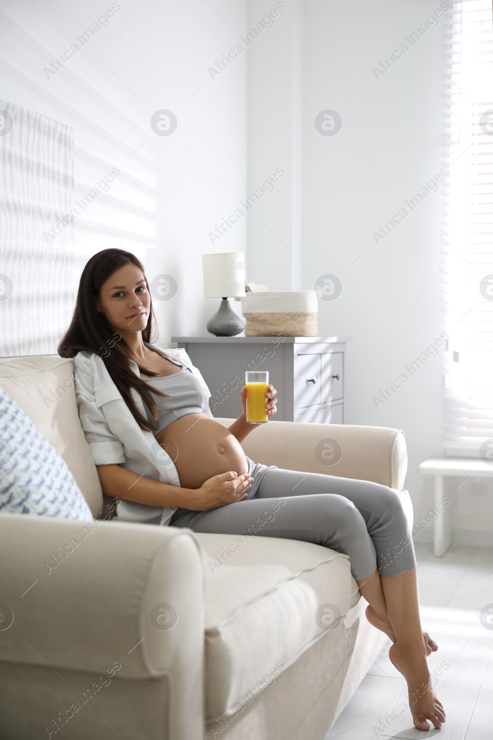 Photo of Young pregnant woman with glass of juice in living room. Taking care of baby health