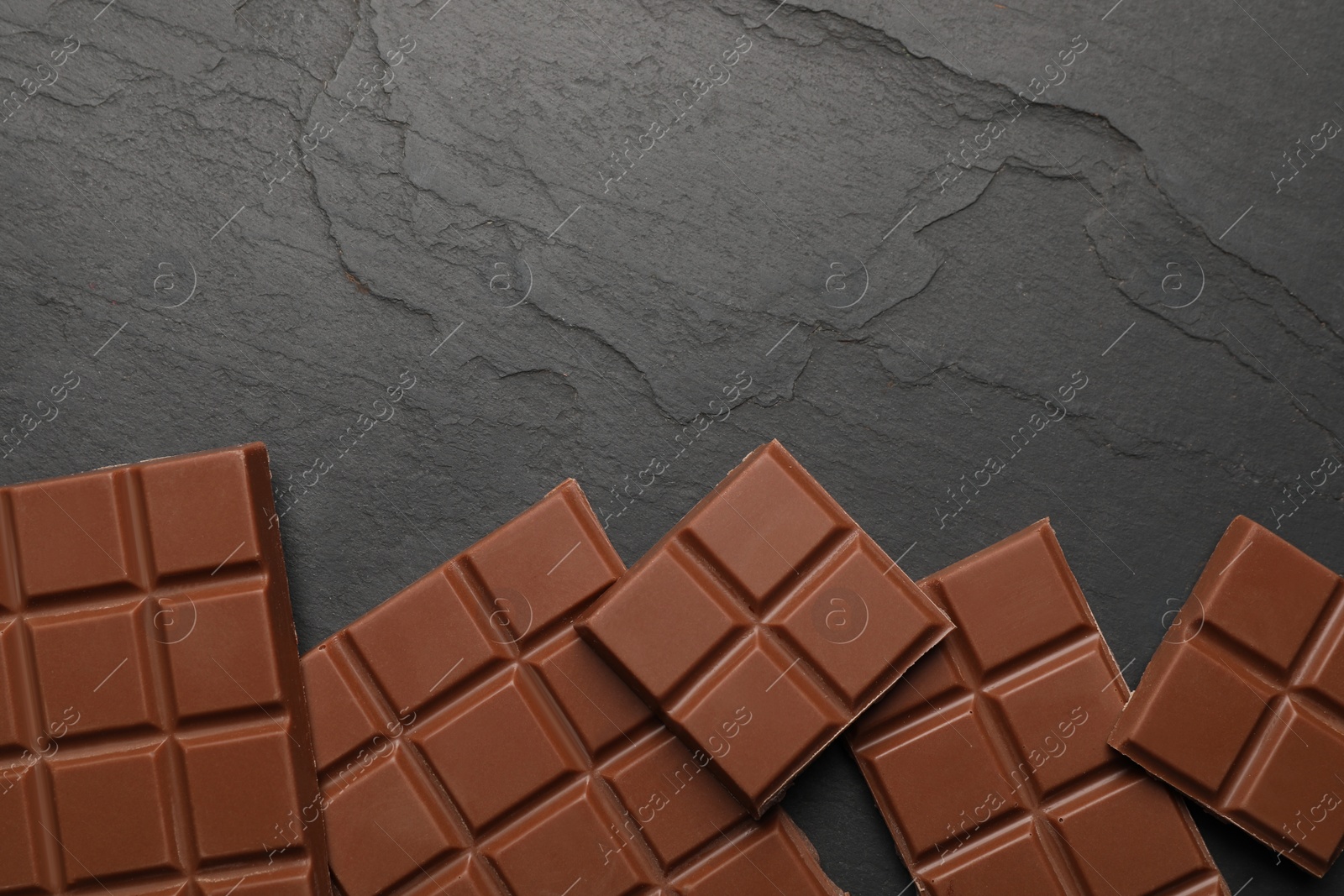 Photo of Delicious milk chocolate on black table, flat lay. Space for text