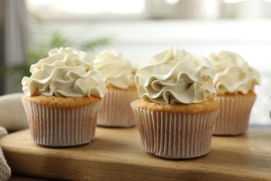 Photo of Tasty cupcakes with vanilla cream on wooden board, closeup