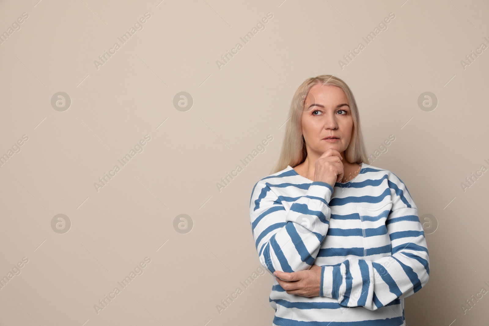 Photo of Thoughtful mature woman on beige background. Space for text