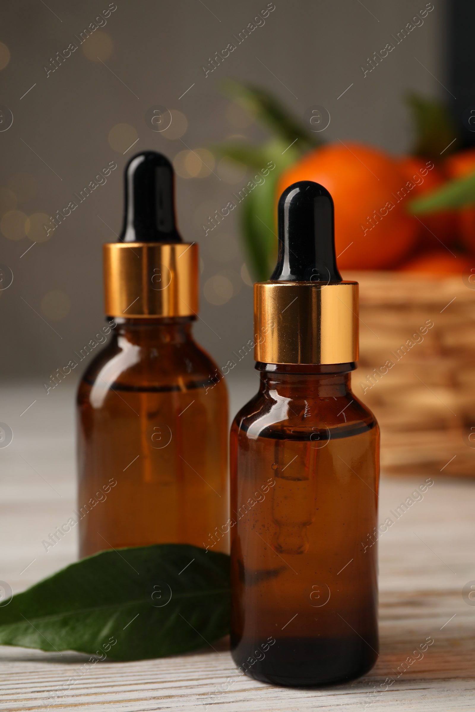 Photo of Bottles of tangerine essential oil and green leaf on white wooden table, closeup